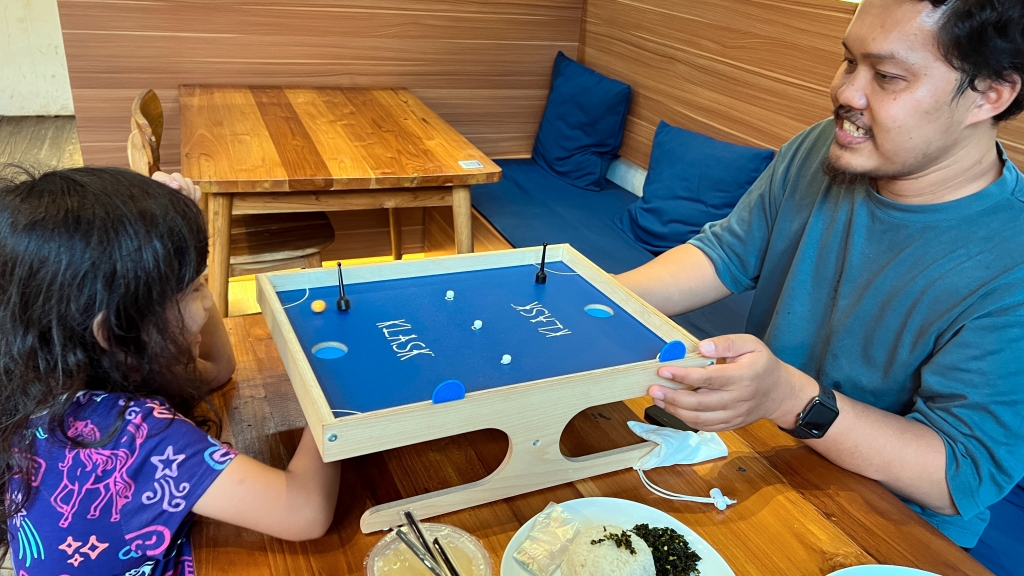 A little girl in purple graphic dress playing Klask board game with a man in a dark blue t-shirt.